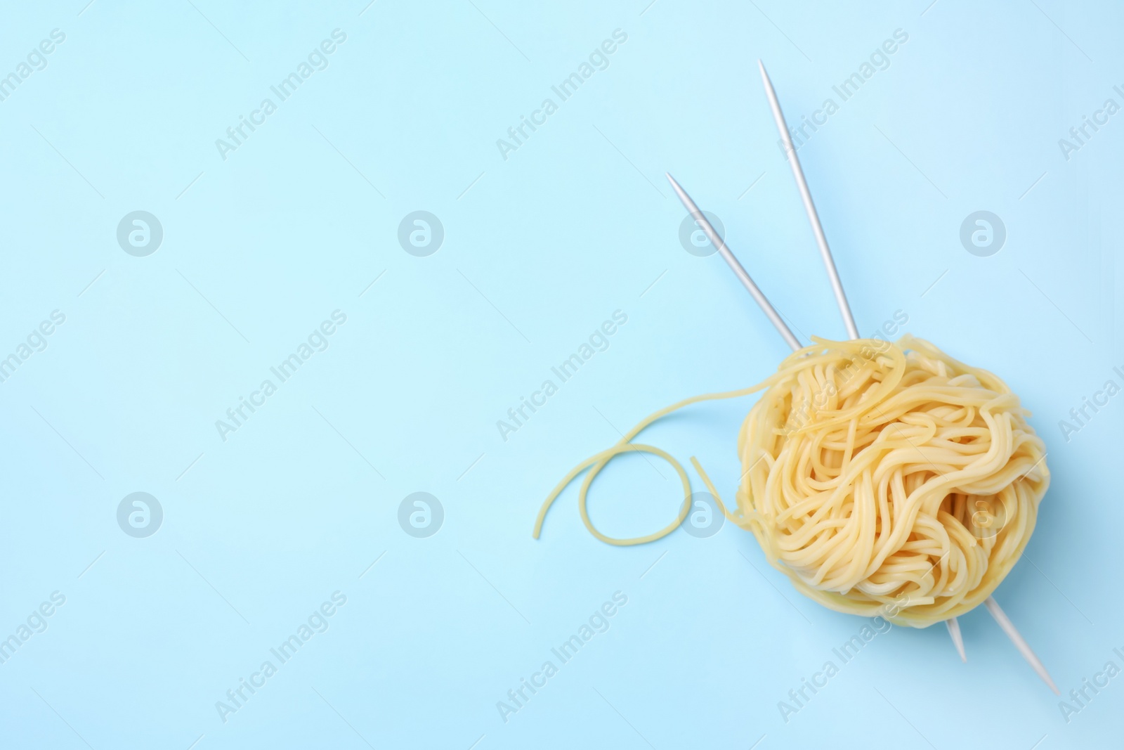 Photo of Pasta as clew with knitting needles on light blue background, top view. Space for text