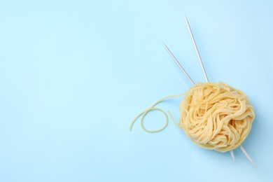 Photo of Pasta as clew with knitting needles on light blue background, top view. Space for text