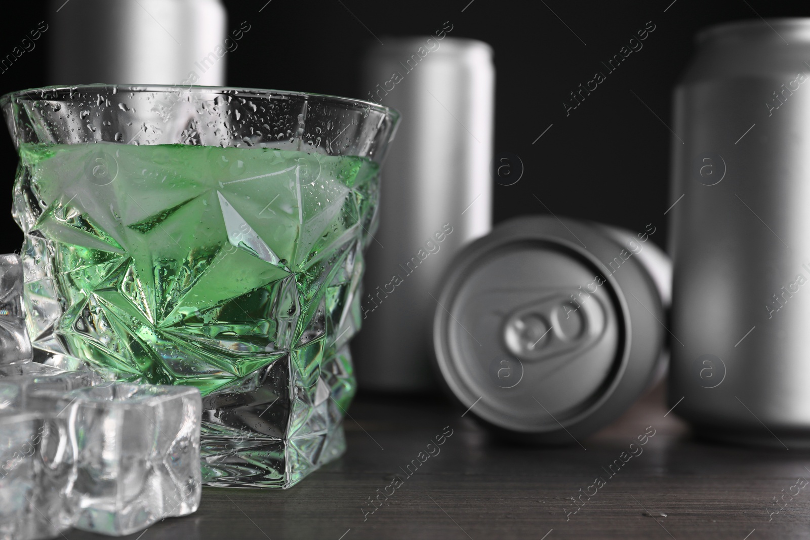 Photo of Energy drink in glass, aluminium cans and ice cubes on wooden table, closeup