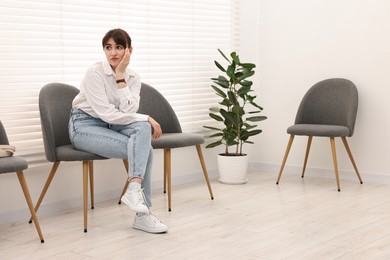 Photo of Woman sitting on chair and waiting for appointment indoors