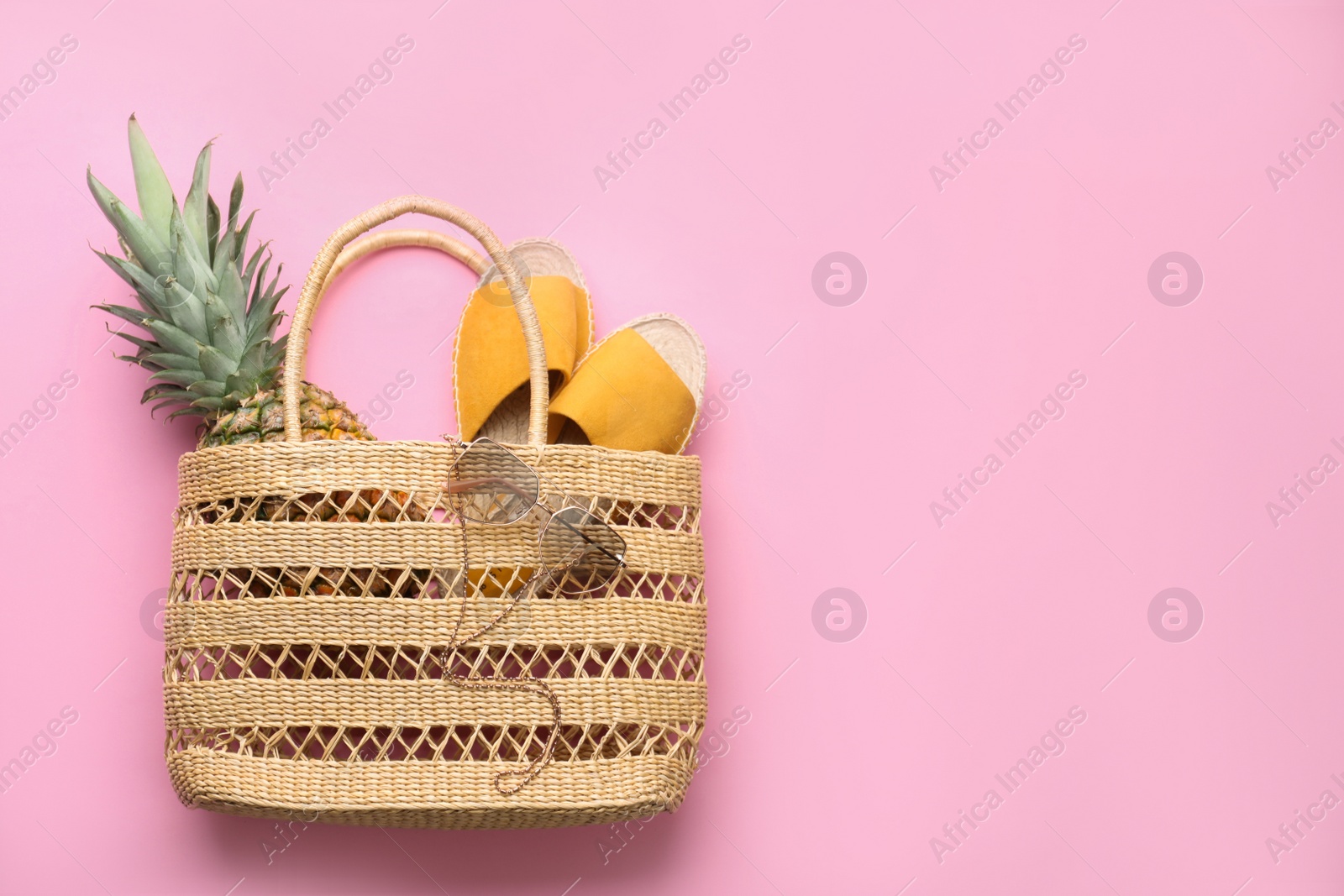 Photo of Elegant woman's straw bag with shoes, sunglasses and pineapple on pink background, top view. Space for text