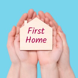 Image of First time home buyer. Woman with her little child holding house figure on light blue background, top view
