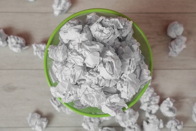 Photo of Full trash bin and crumpled paper on floor, top view