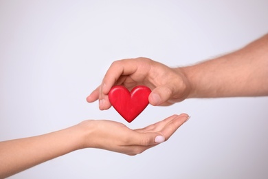 Man giving red heart to woman on white background, closeup. Donation concept