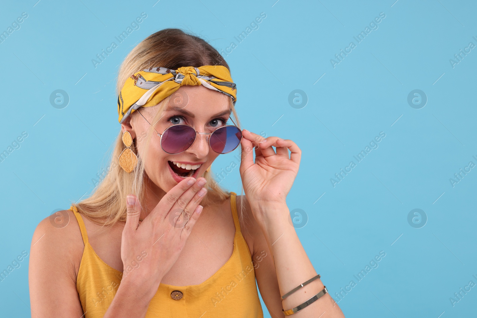 Photo of Portrait of smiling hippie woman in sunglasses on light blue background. Space for text