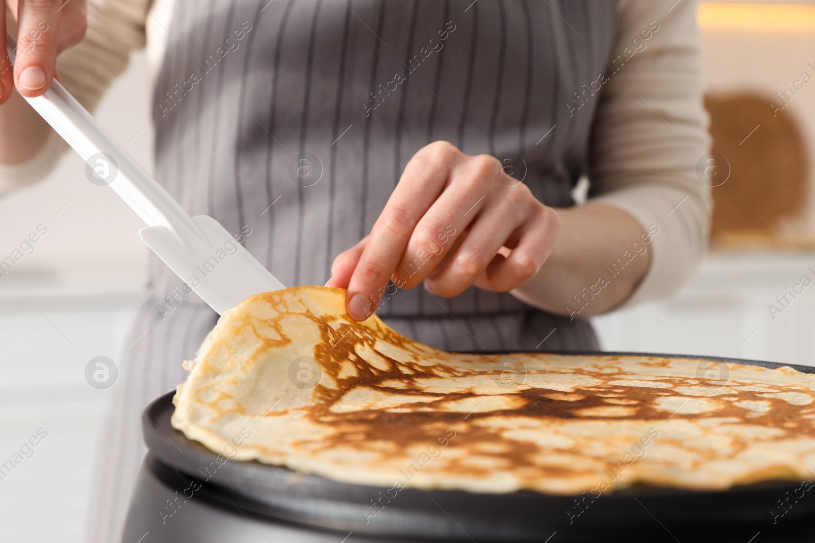 Photo of Woman cooking delicious crepe on electric pancake maker in kitchen, closeup