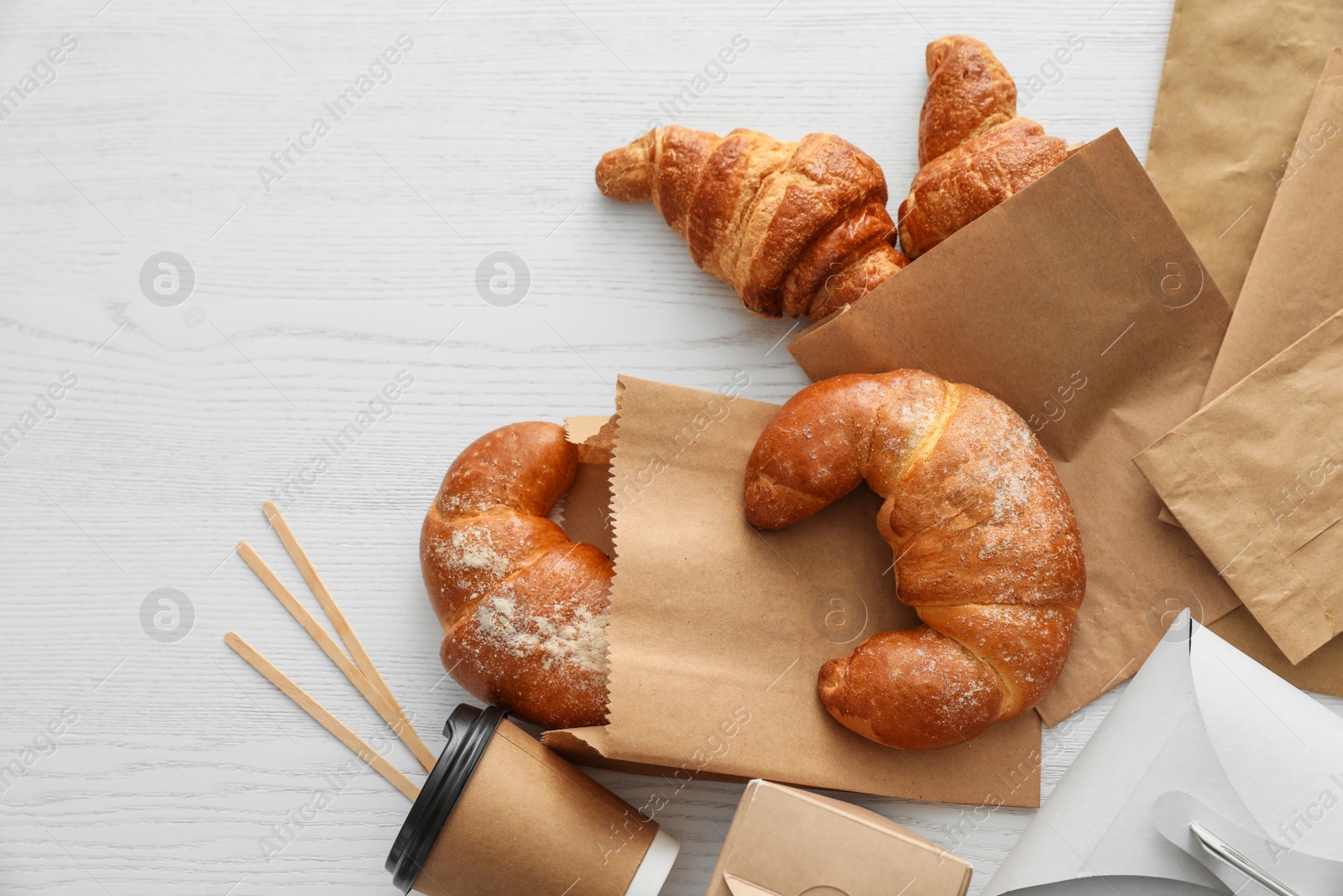 Photo of Flat lay composition with paper bags and pastry on light wooden background. Space for design