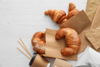 Photo of Flat lay composition with paper bags and pastry on light wooden background. Space for design