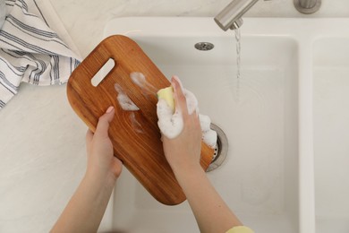 Photo of Woman washing wooden cutting board at sink in kitchen, top view
