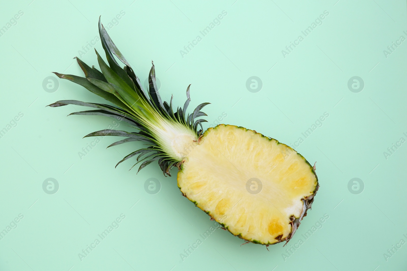 Photo of Half of ripe pineapple on light green background, top view