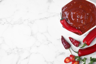Photo of Bowl of hot chili sauce with ingredients on marble background, flat lay. Space for text