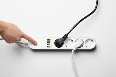 Woman pressing power button of extension cord on white background, top view. Electrician's equipment