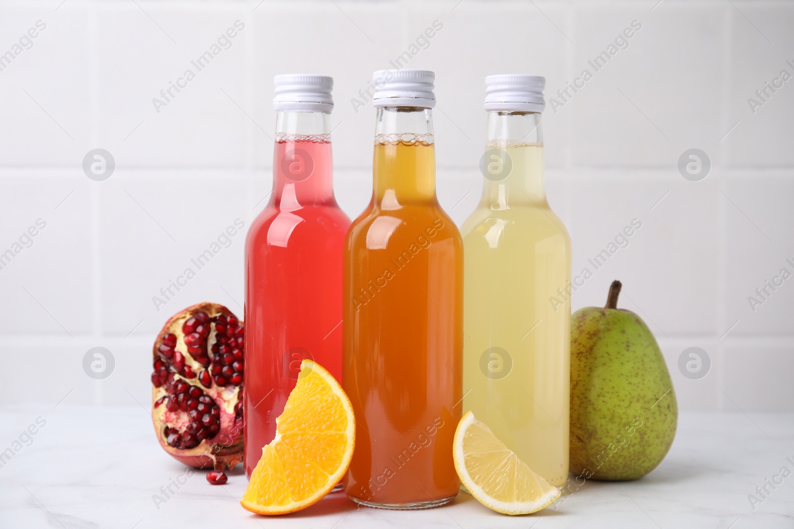 Photo of Delicious kombucha in glass bottles and fresh fruits on white marble table