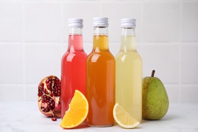 Delicious kombucha in glass bottles and fresh fruits on white marble table