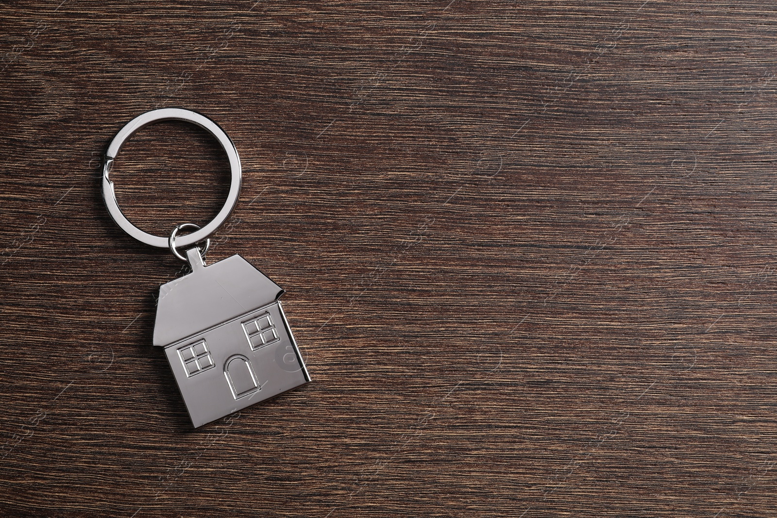 Photo of Metal keychain in shape of house on wooden table, top view. Space for text