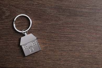 Metal keychain in shape of house on wooden table, top view. Space for text