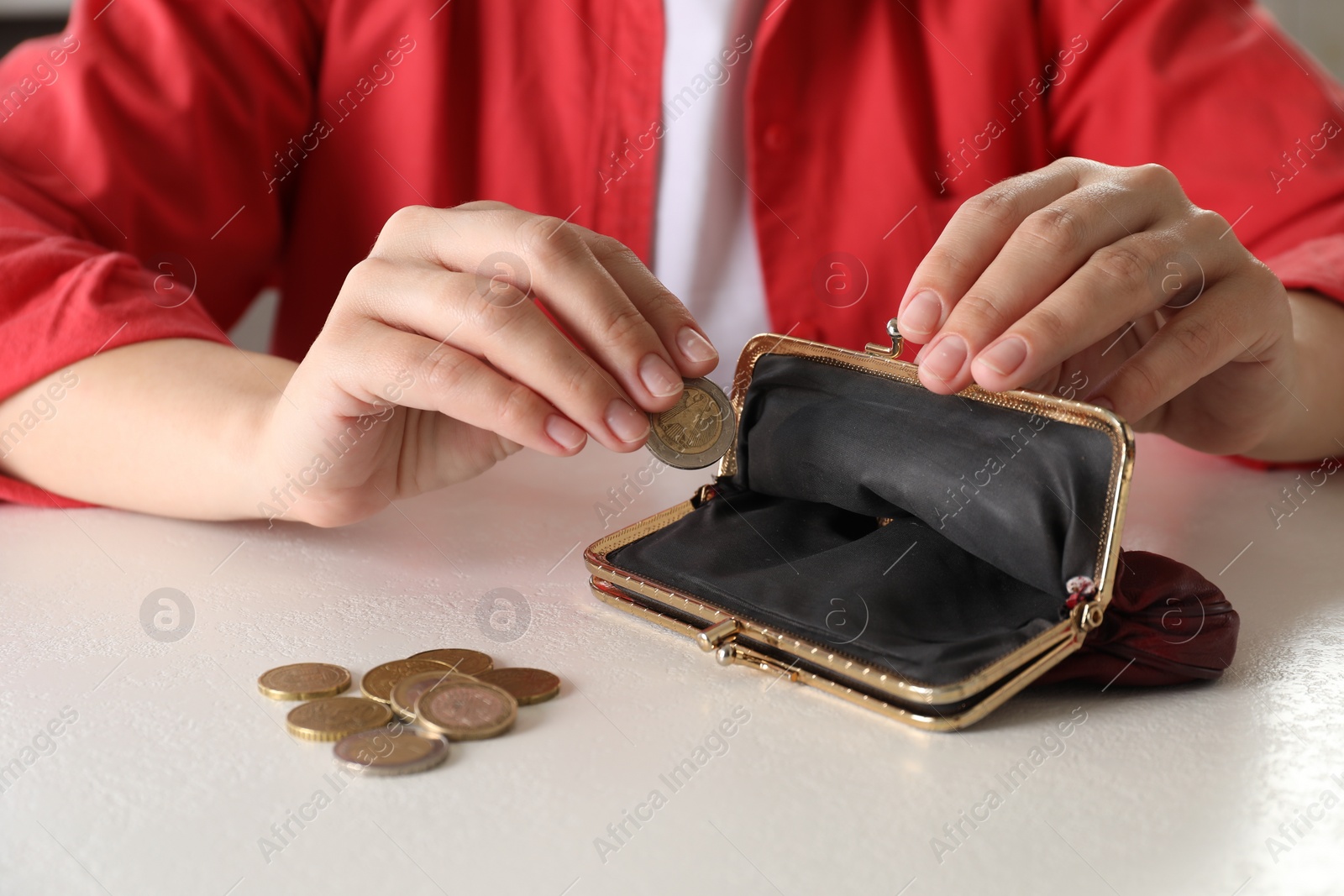 Photo of Poor woman putting coin into empty wallet at white table, closeup