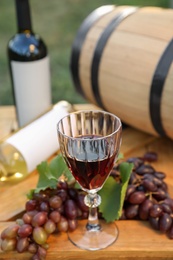 Photo of Composition with wine and ripe grapes on wooden table in vineyard