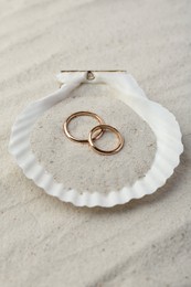 Honeymoon concept. Two golden rings and shell on sand