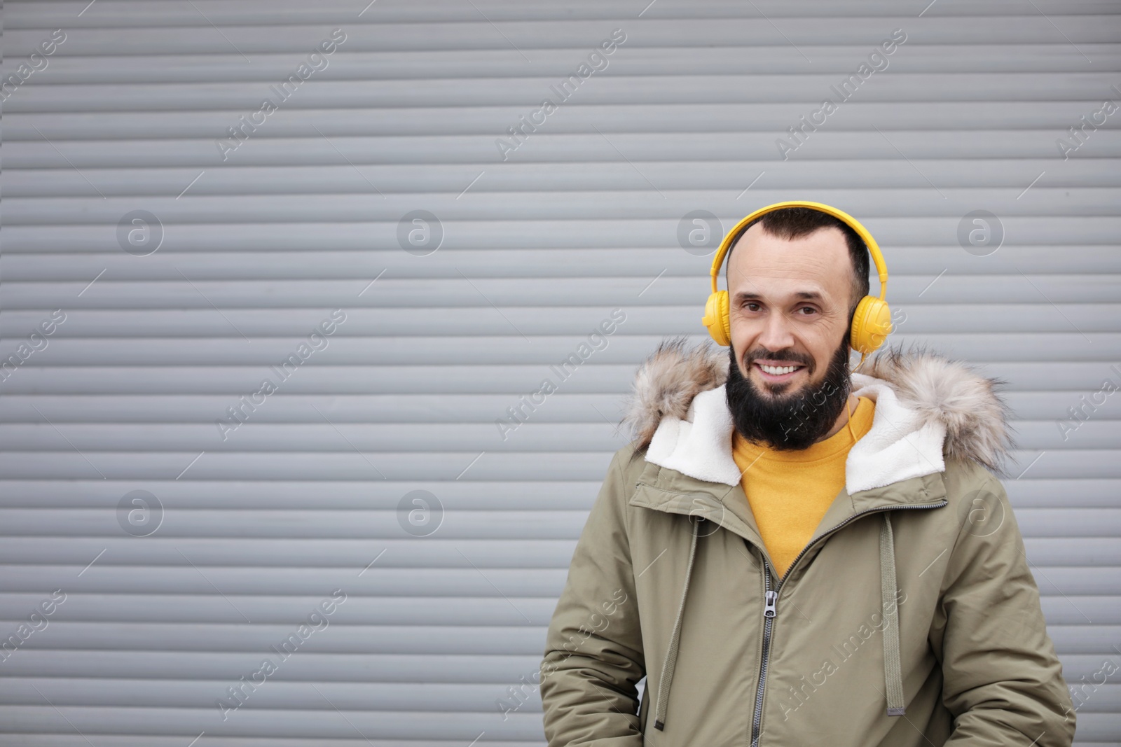 Photo of Mature man with headphones listening to music near light wall. Space for text