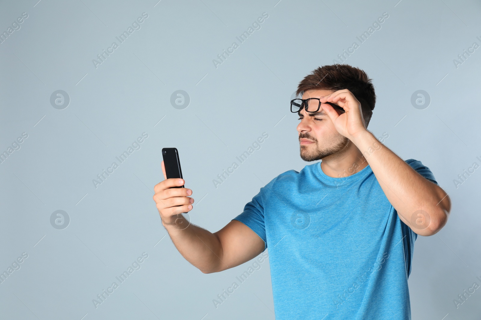 Photo of Young man with vision problems using smartphone on grey background, space for text