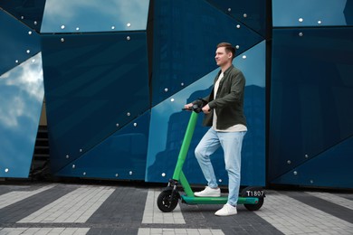 Photo of Happy man with modern electric kick scooter on city street, space for text