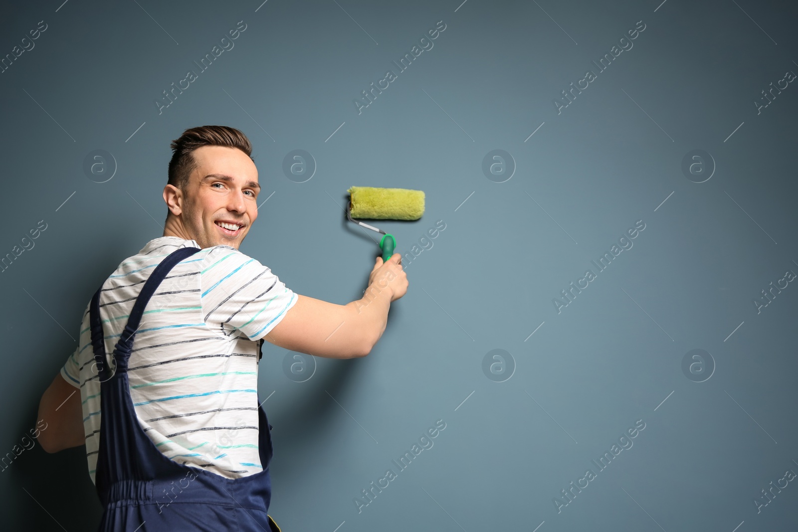 Photo of Young male decorator with paint roller near color wall