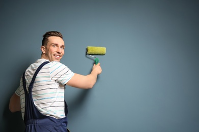 Young male decorator with paint roller near color wall