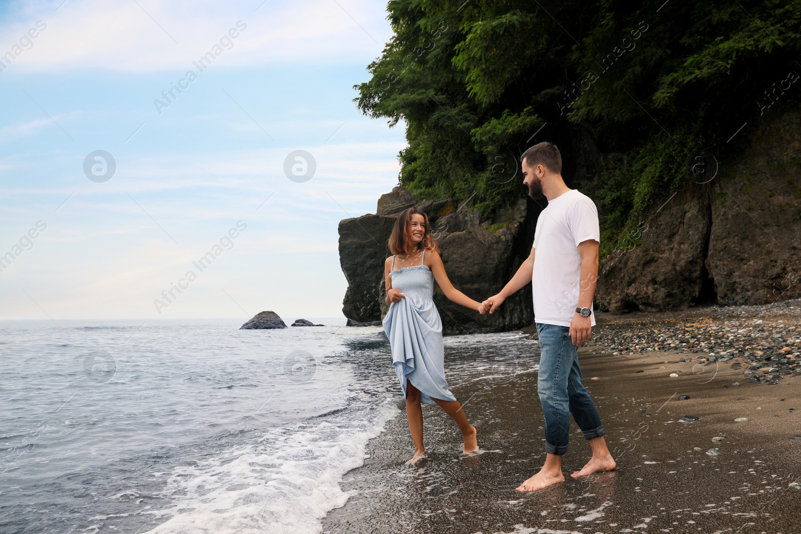 Photo of Happy young couple walking on beach near sea. Space for text