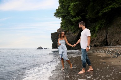 Photo of Happy young couple walking on beach near sea. Space for text