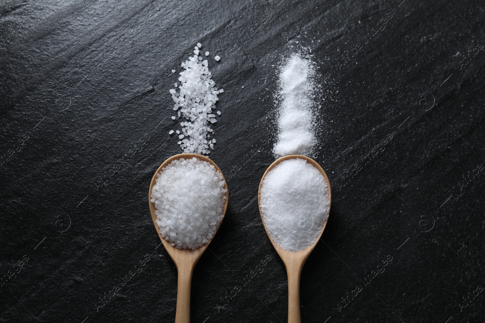 Photo of Organic salt in spoons on black table, flat lay