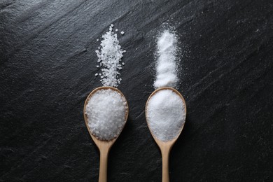 Photo of Organic salt in spoons on black table, flat lay