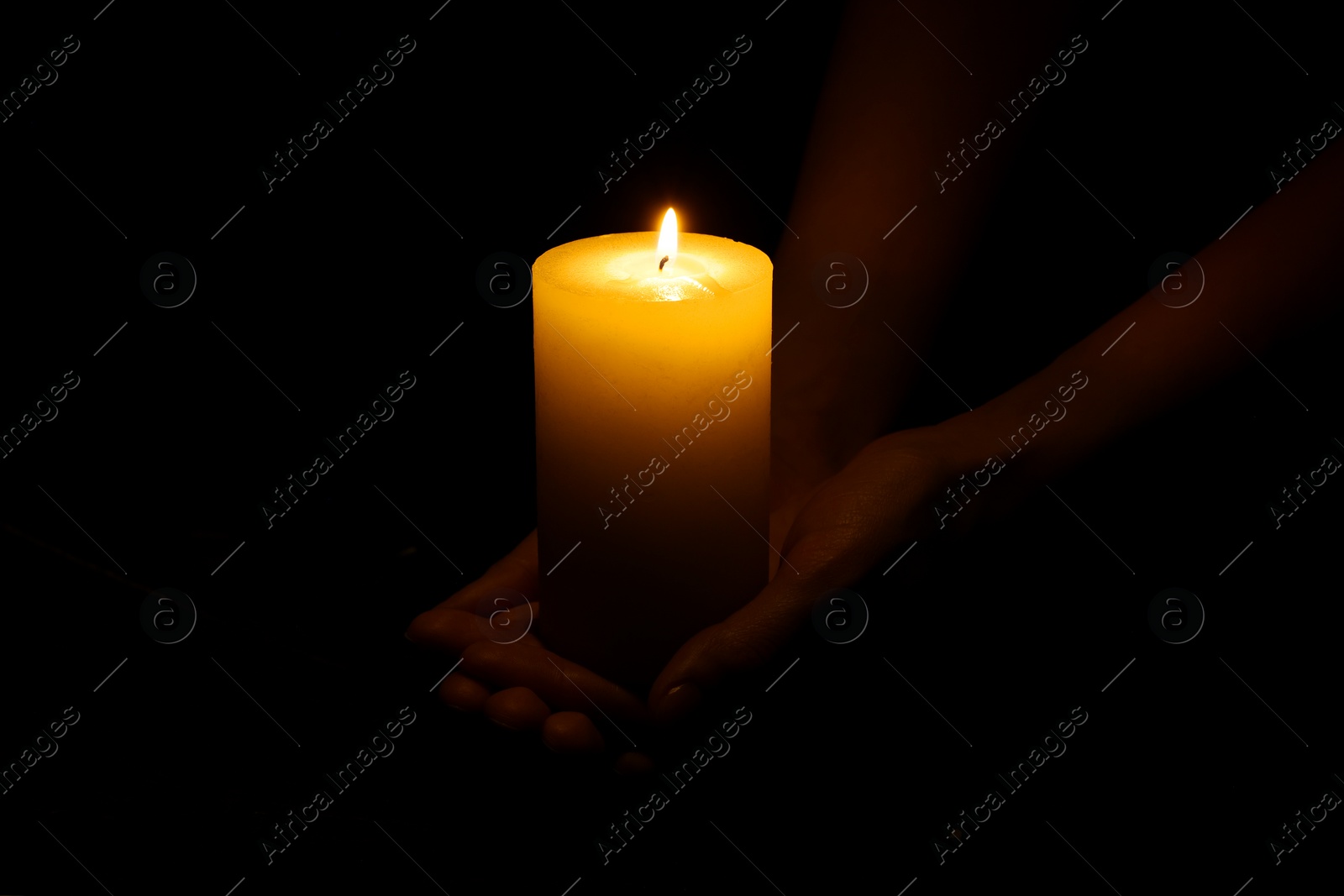 Photo of Woman holding burning candle in hands on black background, closeup