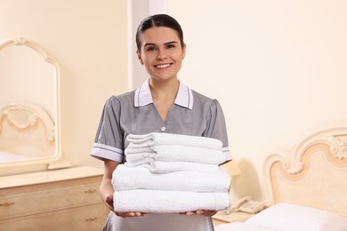 Photo of Young chambermaid holding stack of clean towels in hotel room