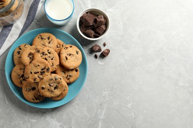 Photo of Delicious chocolate chip cookies and glass of milk on grey marble table, flat lay. Space for text