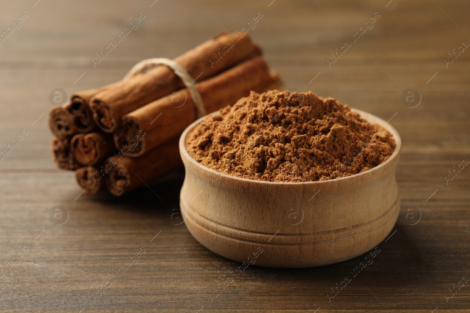 Photo of Aromatic cinnamon powder and sticks on wooden table, closeup