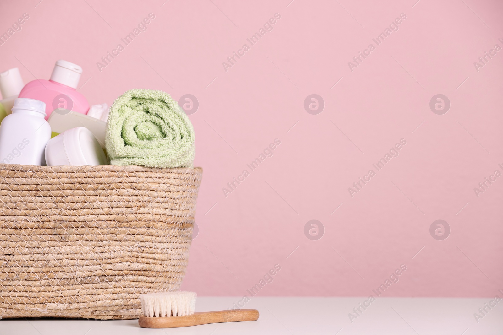 Photo of Wicker basket with baby cosmetic products and bath accessories on white table against pink background. Space for text