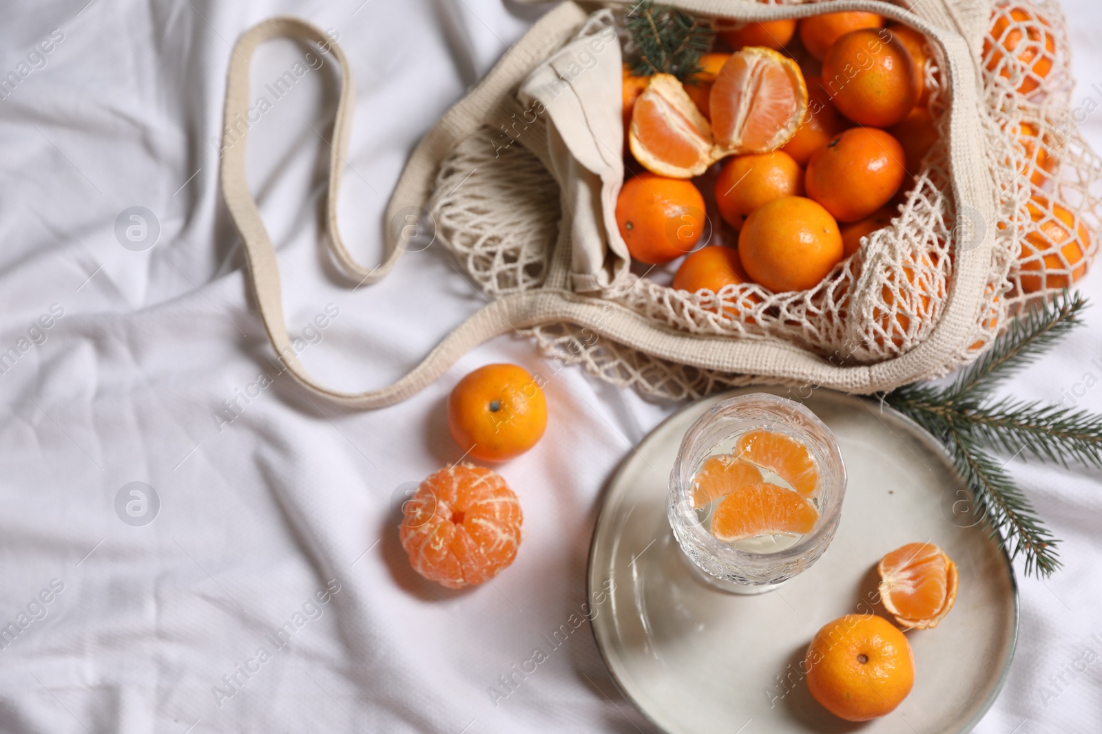 Photo of Delicious ripe tangerines, glass with sparkling wine and fir branch on white bedsheet, flat lay