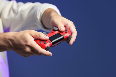 Photo of Man playing video game with controller on dark blue background, closeup. Space for text