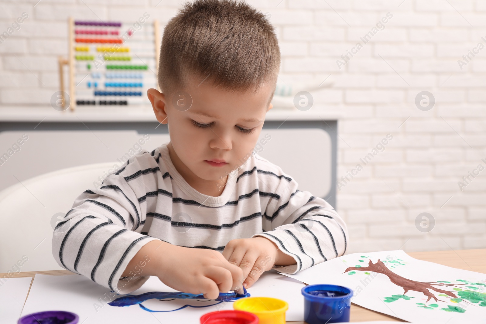 Photo of Little boy painting with finger at wooden table in room