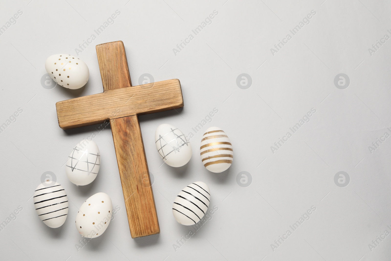 Photo of Wooden cross and painted Easter eggs on light grey background, flat lay. Space for text