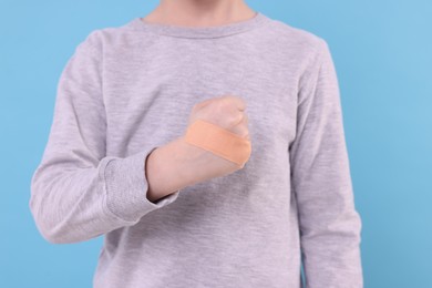 Little boy with sticking plaster on hand against light blue background, closeup