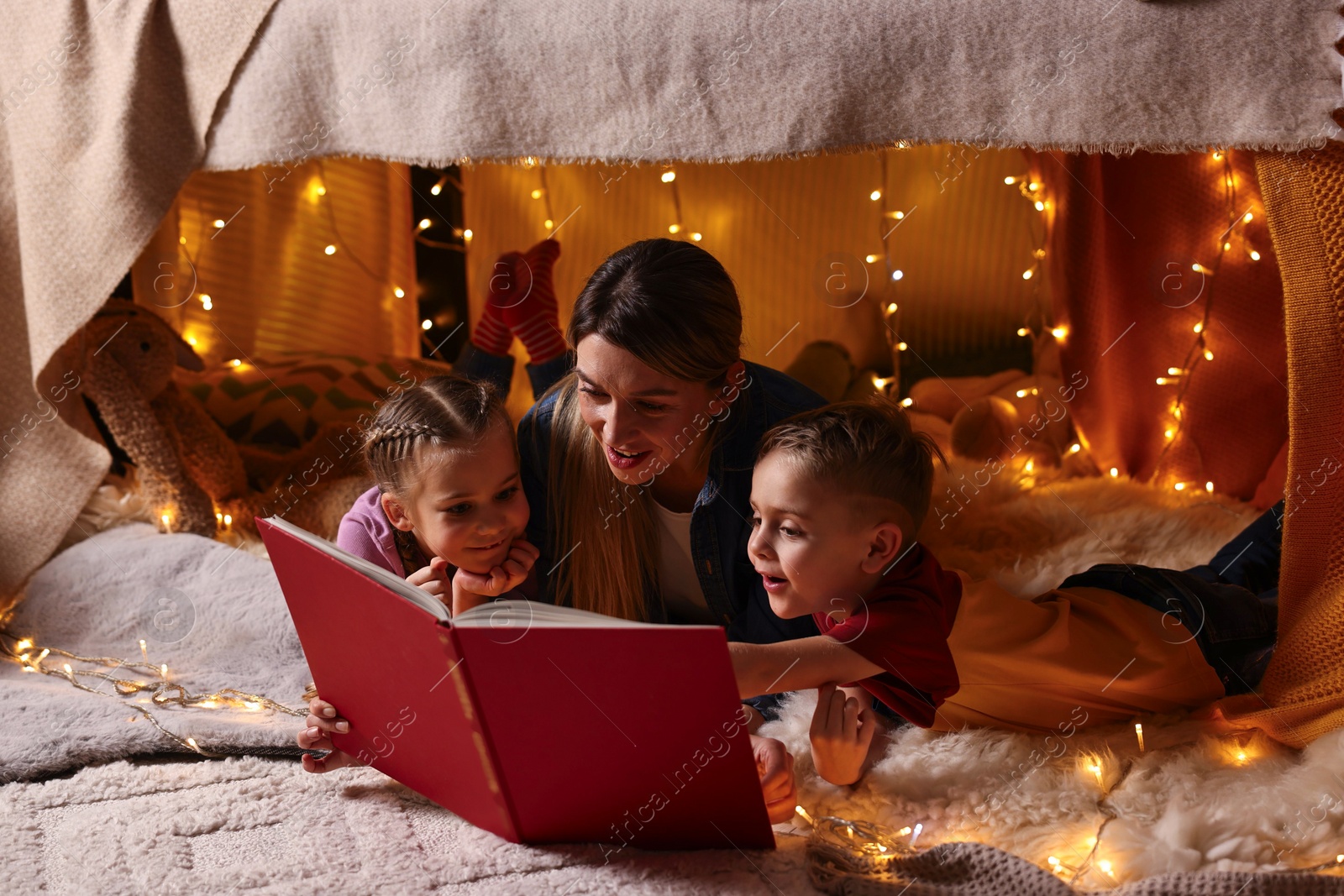 Photo of Mother and her children reading book in play tent at home