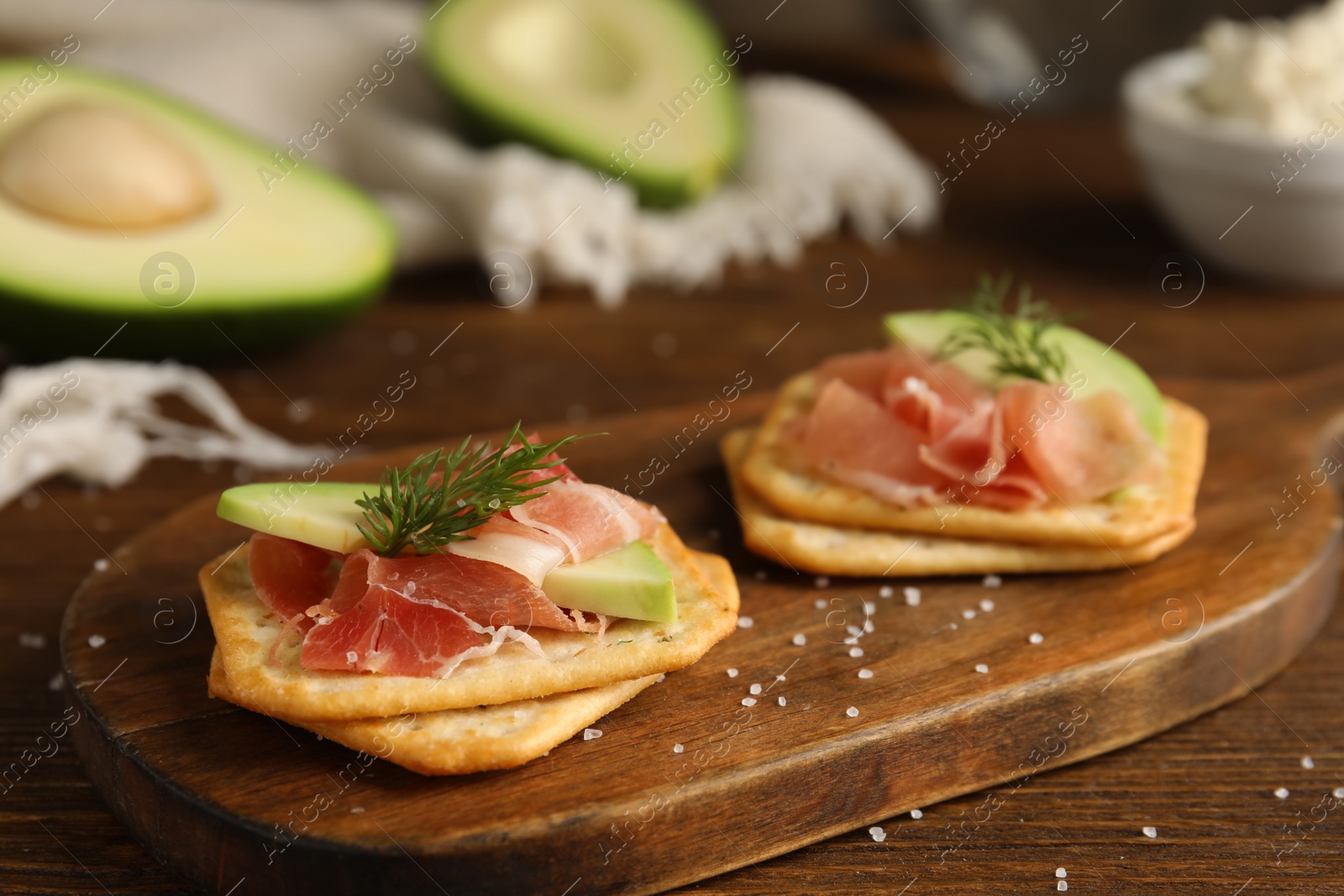 Photo of Delicious crackers with avocado, prosciutto and dill on wooden table, closeup