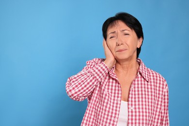 Senior woman suffering from ear pain on light blue background. Space for text