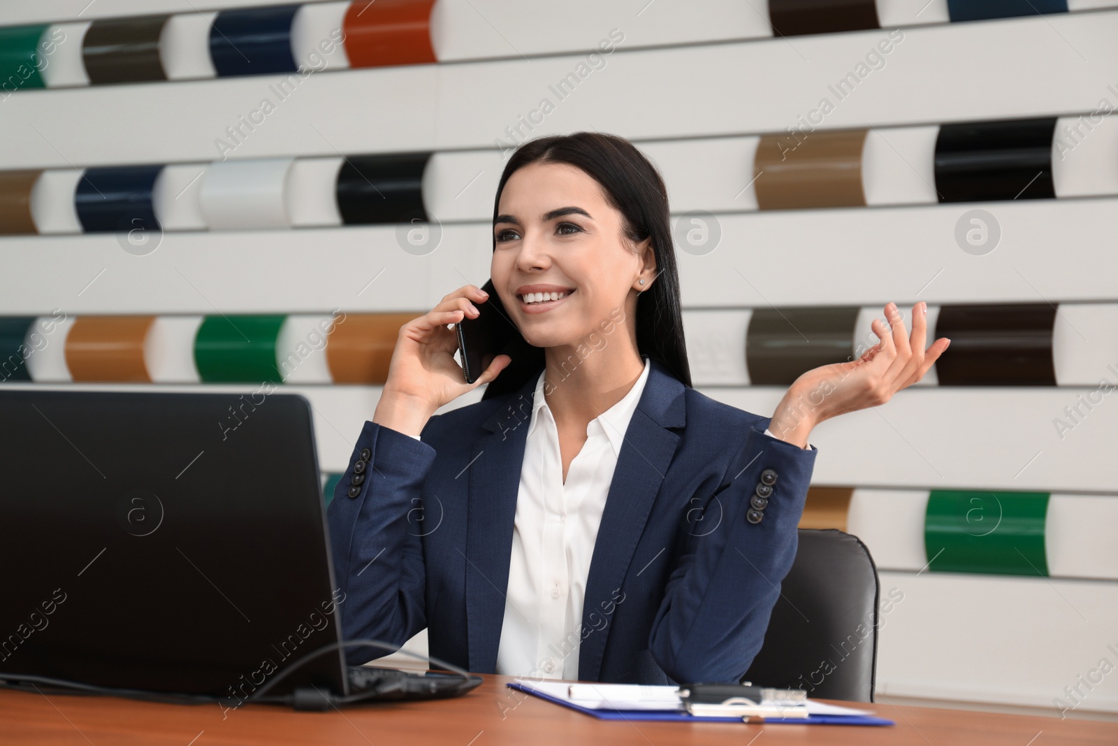 Photo of Saleswoman talking on phone at desk in car dealership