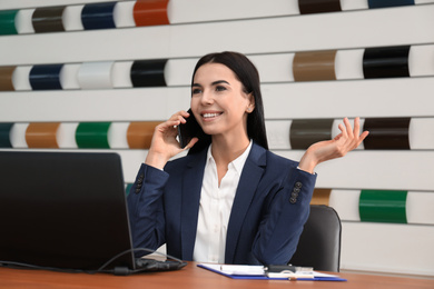 Photo of Saleswoman talking on phone at desk in car dealership