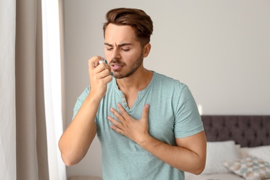 Young man using asthma inhaler at home