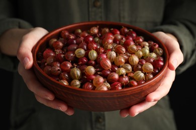 Woman holding bowl full of ripe gooseberries, closeup