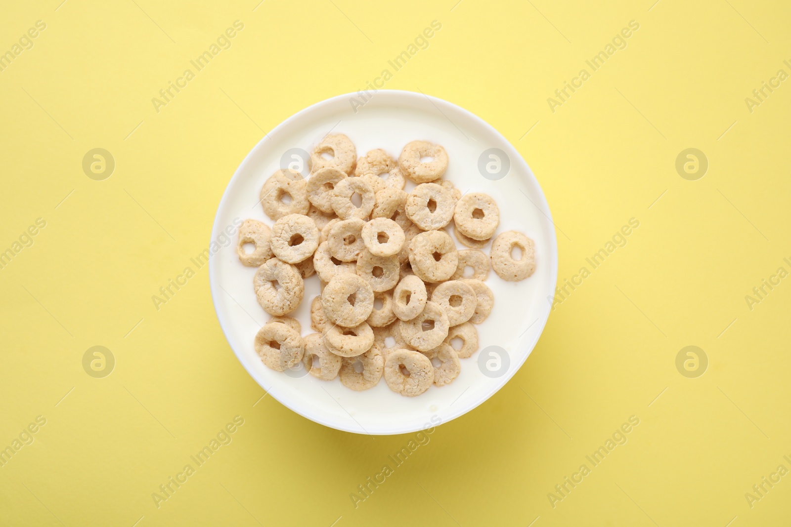 Photo of Breakfast cereal. Tasty corn rings with milk in bowl on yellow background, top view